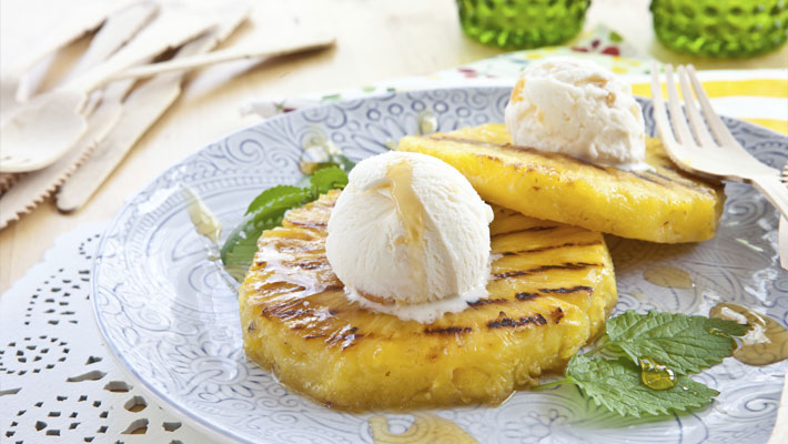 grilled pineapple with ice cream on top and mint leaves and syrup